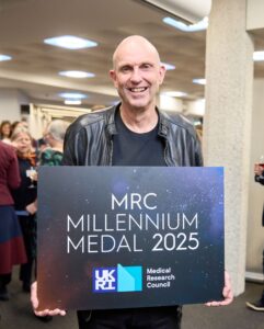 Professor George Davy Smith holding a sign saying “MRC Millennium Medal 2025”