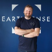 Roland Leigh, Technical Director of Earthsense Ltd, standing in front of a wall featuring the Earthsense logo
