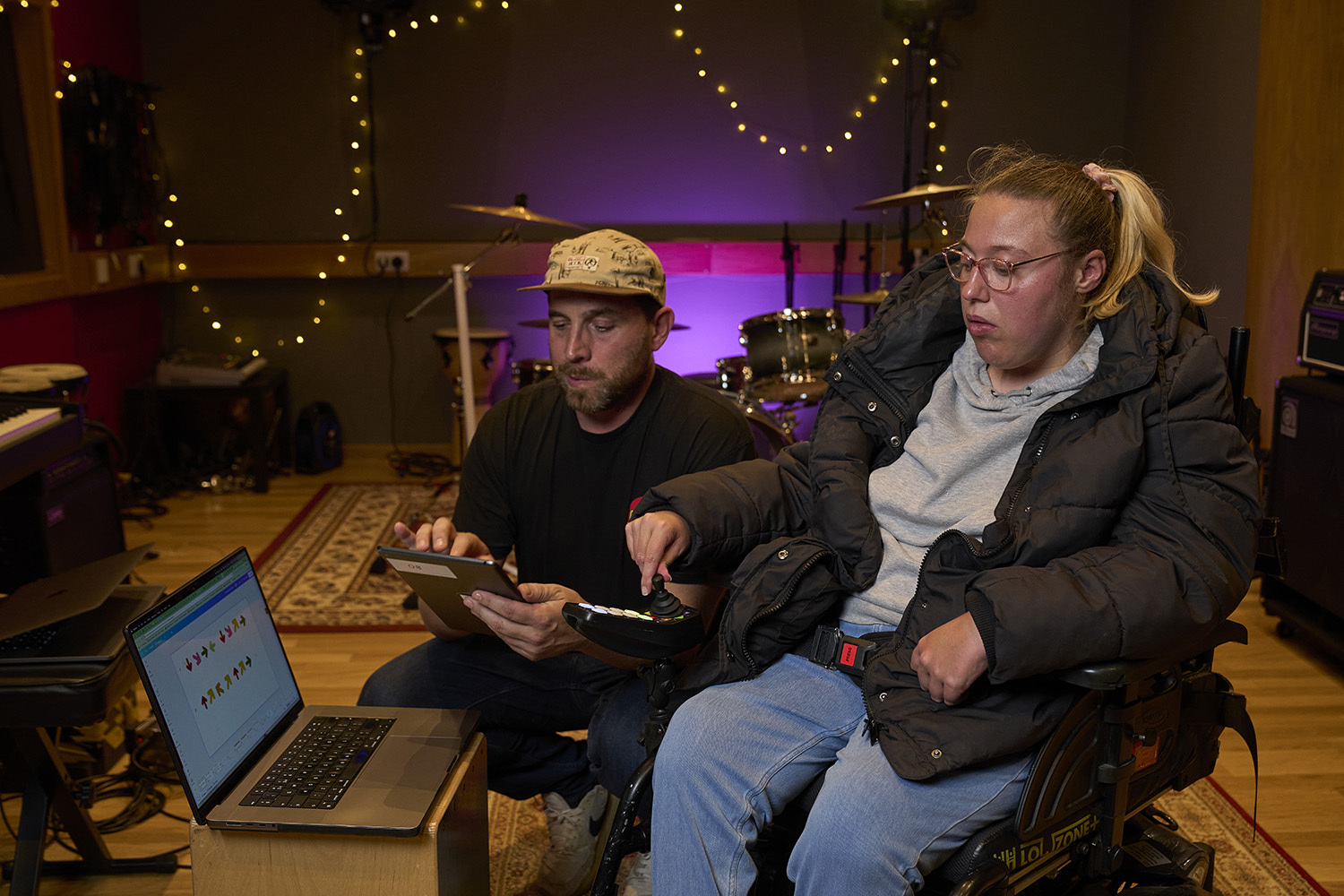 A female wheelchair user demonstrates a controller in a music studio.